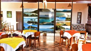 A restaurant with tables set for dining, featuring a large window with a view of a coastal landscape.