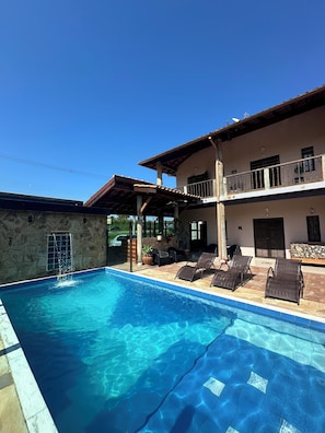 Una piscina con sillones de descanso y un muro de piedra.