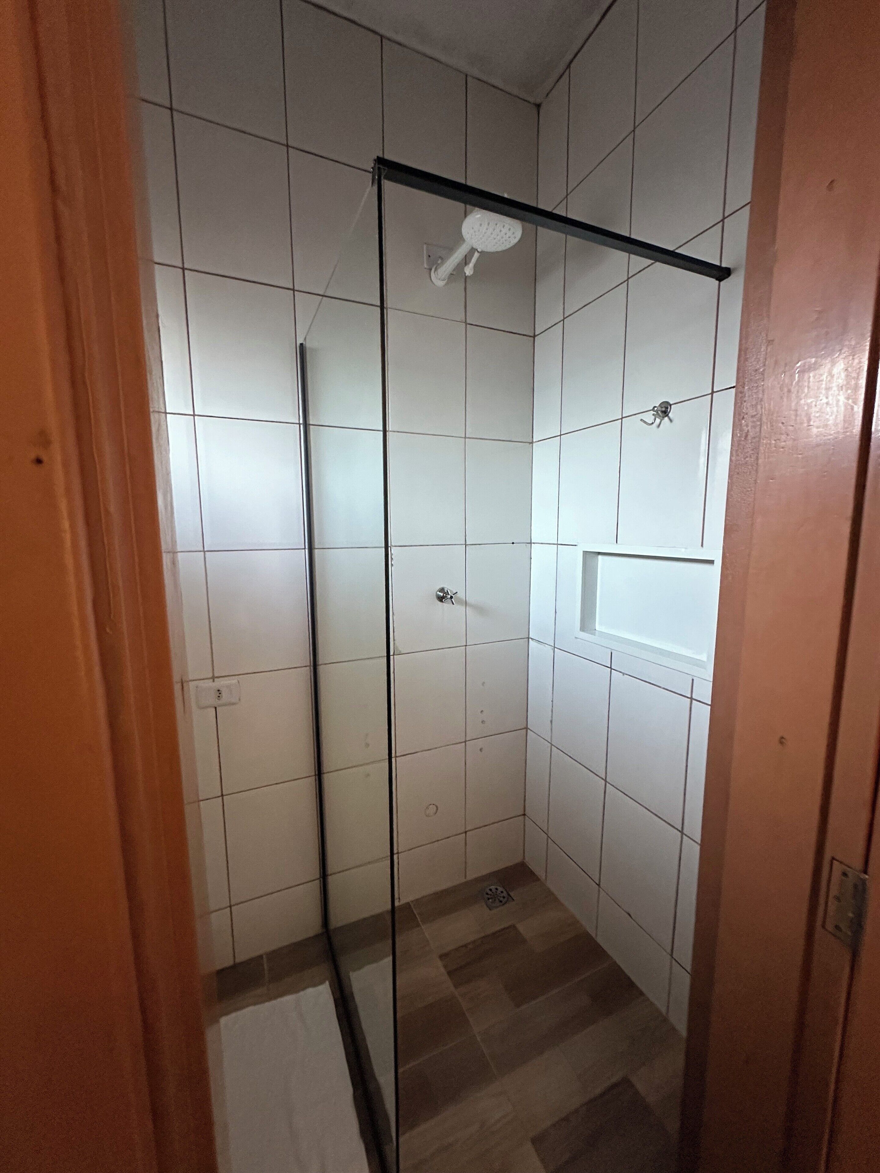 A small, tiled bathroom with a glass shower enclosure, a white sink, and a tiled floor.