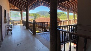 A covered outdoor area with tiled flooring, wooden railings, and a view of a distant building and hills.