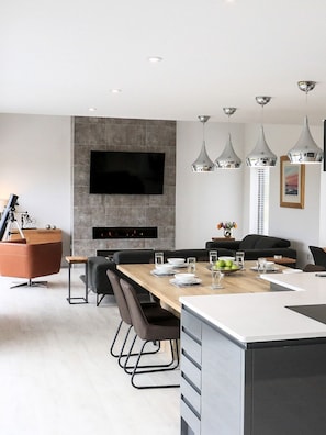 A modern kitchen with a large island, a dining area with a long table, and a mounted flat-screen TV.