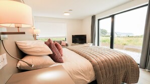 Moderni hotellihuone, jossa on suuri sänky, litteänäyttöinen televisio ja liukuovesta avautuva näkymä ulos.
