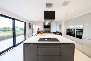 A modern kitchen with a large island, built-in appliances, and a view through large windows.