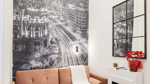 A living room with a pink sofa, a round wooden coffee table, a fireplace, and a large cityscape mural on the wall.