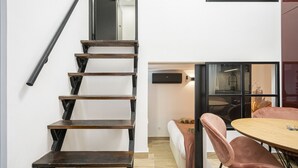 A staircase with wooden steps and a metal handrail, leading to a room with a bed and a round table with chairs.