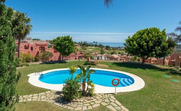 Une piscine entourée d’un chemin pavé de pierres, avec vue sur un terrain de golf et des bâtiments en arrière-plan.