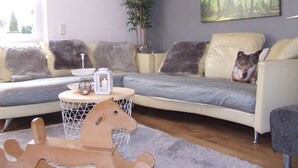 A modern living room with a sofa, a small round table, a decorative horse sculpture, and a large forest-themed painting on the wall. - Hochwald vacation apartment - in the heart of the Saarland (Quierschied)