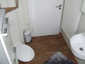 A small bathroom with a toilet, a sink, and a trash can.