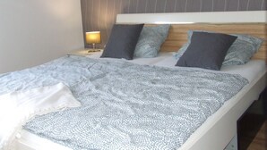 A neatly made bed with a patterned blanket, a bedside lamp, and a headboard with vertical lines. - Hochwald vacation apartment - in the heart of the Saarland (Quierschied)