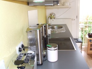 A compact kitchen with a coffee maker, a kettle, and a jar on the counter.