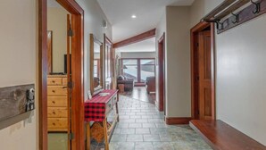 A hallway with wooden doors, a checkered table, and a view into a living area. - Mountain Time-Spacious, Private Hot Tub,Great View (Big White)