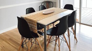Un comedor con una mesa, sillas, una lámpara colgante tejida y una obra de arte en la pared.