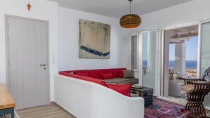 Moderni olohuone, jossa on punainen sohva, suuri abstrakti maalaus ja lasiovesta avautuva näkymä merelle.
