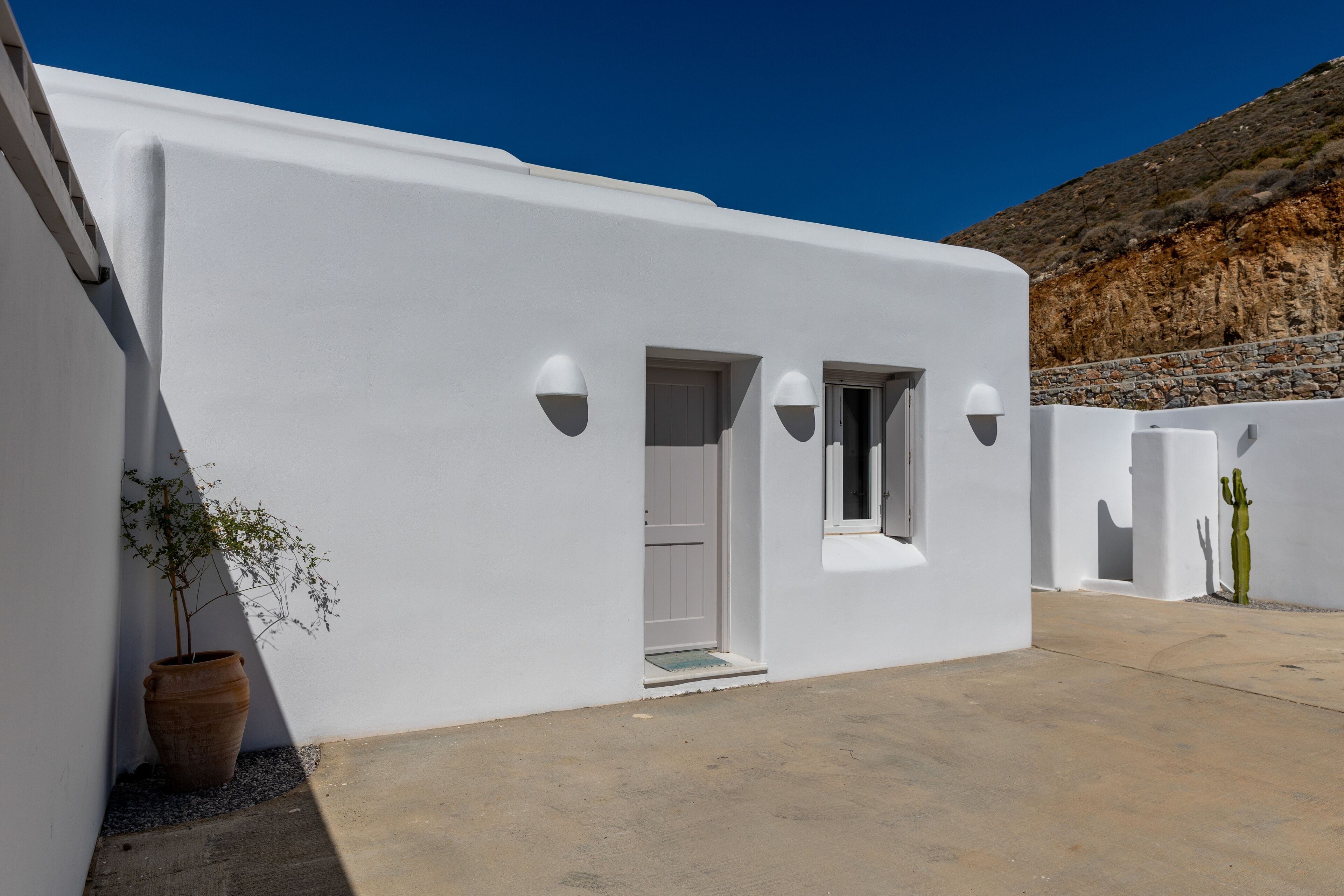 A white building with a door and windows, a potted plant, and a statue.