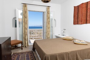 A bedroom with a bed, a chair, a dresser, a sink, and a view of the sea.