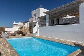 A modern white villa with a swimming pool, stone flooring, and outdoor seating.