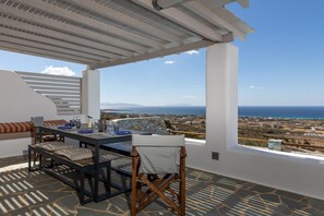 A dining area with a table and chairs, a bench, and a view of the sea and landscape.