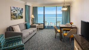 A hotel room with a sofa, a dining table with chairs, a TV, and a balcony with a view of the ocean. - Family Suite at Coral Beach Resort - Full Access to Amenities! (Myrtle Beach)