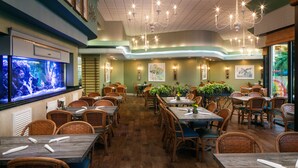 A restaurant with wooden tables and wicker chairs, a large aquarium on the left, and wall-mounted lights. - Family Suite at Coral Beach Resort - Full Access to Amenities! (Myrtle Beach)