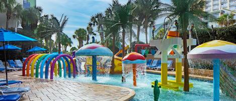 Zona de piscina con fuentes de agua coloridas y sillas de descanso.