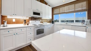 A modern kitchen with white cabinets, a large island, and a view of the beach through the window.