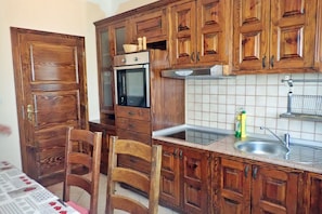 A kitchen with wooden cabinets, a built-in oven, a sink, and a dining table with chairs. - Villa in Starigrad near Paklenica National Park (Starigrad Paklenica)