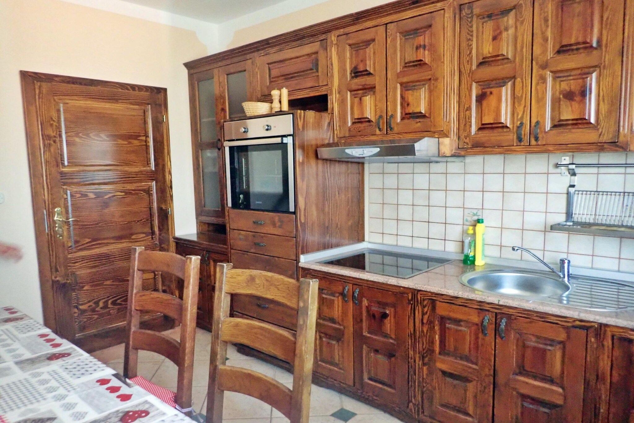 A kitchen with wooden cabinets, a built-in oven, a sink, and a dining table with chairs.