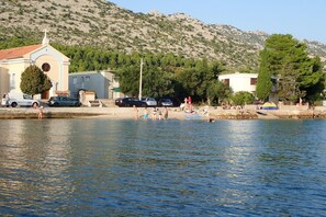 A waterfront scene with a building, parked cars, and people by the water. - Villa in Starigrad near Paklenica National Park (Starigrad Paklenica)