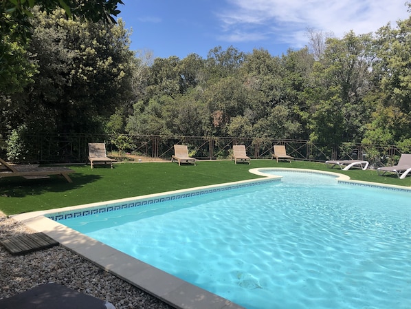 A swimming pool with a clear blue water, surrounded by a grassy area and trees.