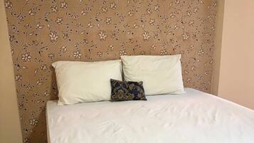 A hotel room with a bed, a decorative headboard, a wall-mounted air conditioner, and a neatly made bed with a patterned bedspread and pillows.