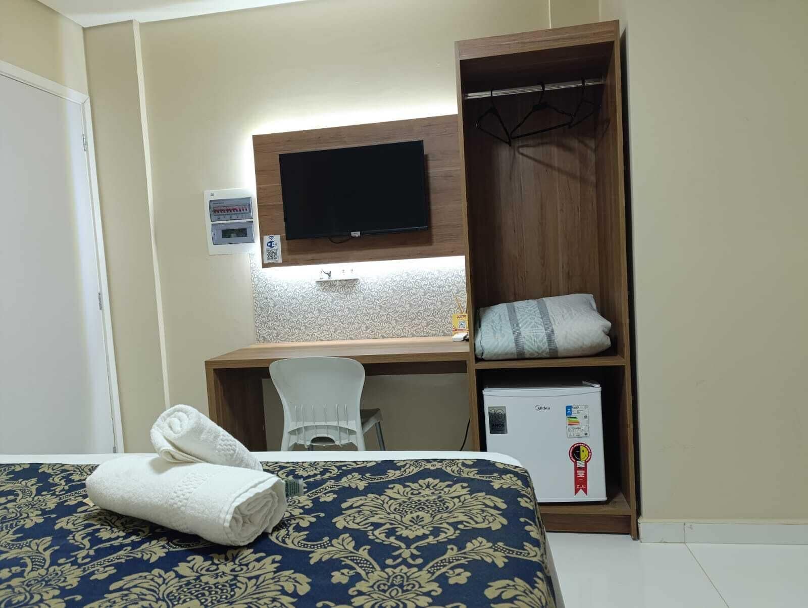 Hotelkamer met een bed, een bureau met een computer, een televisie, een kledingkast en een koelkast.
