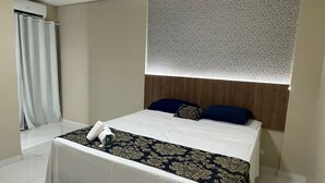 A hotel room with a neatly made bed, a wooden headboard, a patterned bedspread, and a window with a patterned curtain. - Hotel la Sierra (Bodoquena)