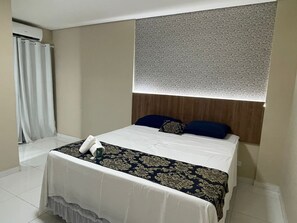 Una habitación de hotel con una cama bien hecha, cabecera de madera, colcha estampada y una ventana con cortina decorada.