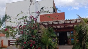 A building with a covered entrance, surrounded by lush greenery and flowering plants. - Hotel la Sierra (Bodoquena)
