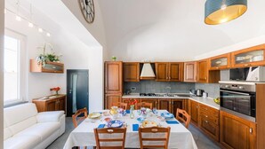 A modern kitchen with wooden cabinets, a dining table set for four, and a built-in oven. - Maika House - Amalfi Coast - seaview (Atrani)