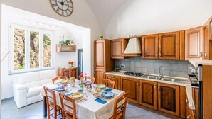 A kitchen with wooden cabinets, a dining table set for four, and a large clock on the wall. - Maika House - Amalfi Coast - seaview (Atrani)
