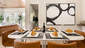 A dining area with a marble table, orange chairs, and a large abstract painting on the wall. - Modern Luxury - Carmel (Carmel-by-the-Sea)
