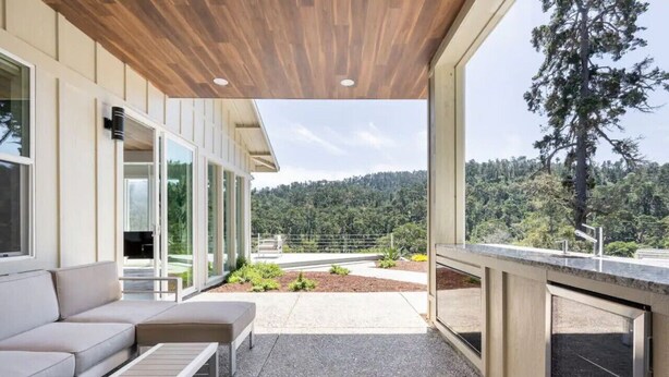 An outdoor patio area with a sofa and a table, a wooden ceiling, and a view of a forested hillside. - Modern Luxury - Carmel (Carmel-by-the-Sea)