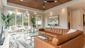 A modern living room with a brown leather sofa, glass coffee table, and white chairs. - Modern Luxury - Carmel (Carmel-by-the-Sea)