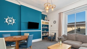 Uma sala de estar com parede azul, uma mesa de madeira, um sofá, uma televisão e uma estante de livros.