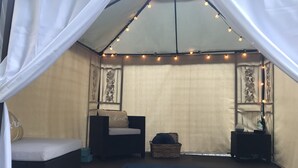 A tented room with two wicker sofas, a blue mat, and string lights.
