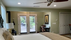 A bedroom with a large bed, a ceiling fan, and a view of the outdoors through a door.