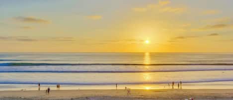 Una playa con un atardecer, olas y gente.