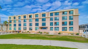 A multi-story hotel with a flat facade, large windows, and a well-maintained lawn in front. - Cozy Oceanfront view, beach access, pool, parking (San Diego)