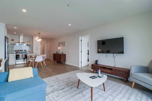 A modern living room with a blue sofa, a white coffee table, and a grey armchair. A flat-screen TV is mounted on the wall. - Cozy Oceanfront view, beach access, pool, parking (San Diego)