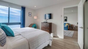 A bedroom with a large bed, a television, a dresser, and a view of the sky through a window. - Cozy Oceanfront view, beach access, pool, parking (San Diego)