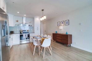 A modern kitchen with stainless steel appliances, a dining area with a wooden table and white chairs, and a wooden cabinet with decorative items.