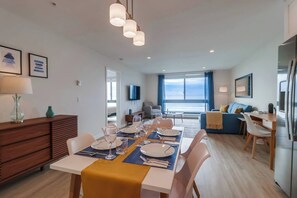 Un espace de repas moderne avec une table dressée pour quatre personnes, un canapé et une vue sur la mer.