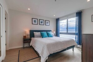 Une chambre à coucher avec un lit, une table de chevet, une fenêtre avec des rideaux et des tableaux encadrés accrochés au mur.