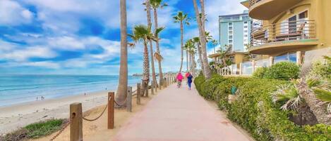 Un paseo marítimo frente a la playa bordeado de palmeras y un edificio con balcones que dan al océano.